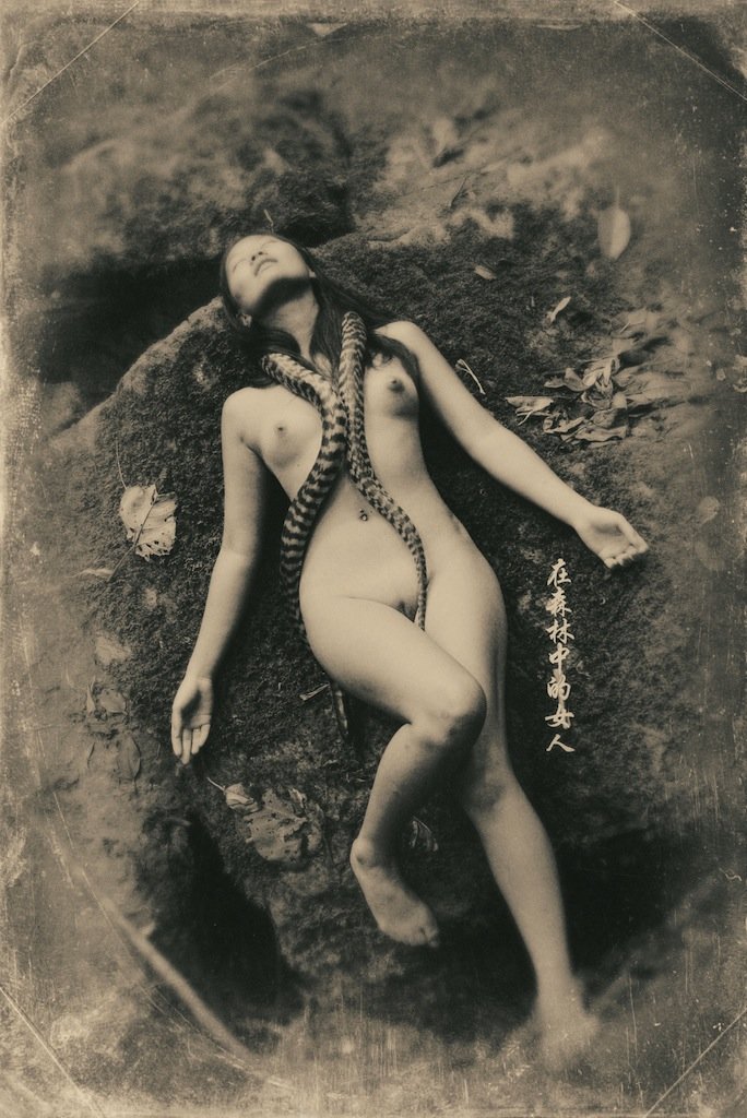 Asian nude resting with one or more snakes wrapped around her neck